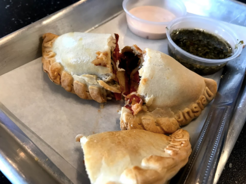 A tray with two halves of a golden-brown empanada, accompanied by dipping sauces in small containers.