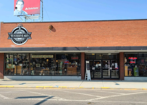 Exterior of Yesteryears Antiques store, featuring large windows displaying various antiques and a neon "Open" sign.