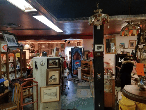 A cozy antique shop filled with various vintage items, furniture, and decorative pieces, with warm lighting.