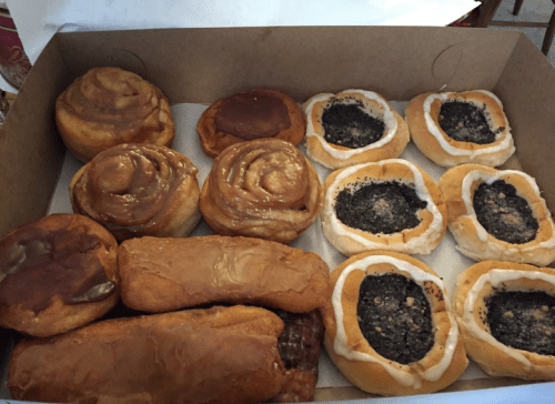 A box filled with assorted pastries, including cinnamon rolls, poppy seed rolls, and glazed donuts.