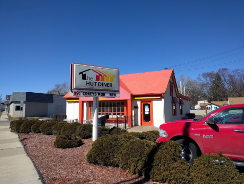 A diner with a red roof and sign, surrounded by shrubs and a red truck parked nearby.