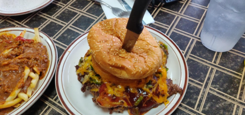 A large burger with melted cheese and toppings, served on a plate with a knife inserted through the bun.
