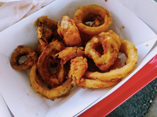 A box filled with crispy, golden-brown onion rings, some whole and others in pieces.