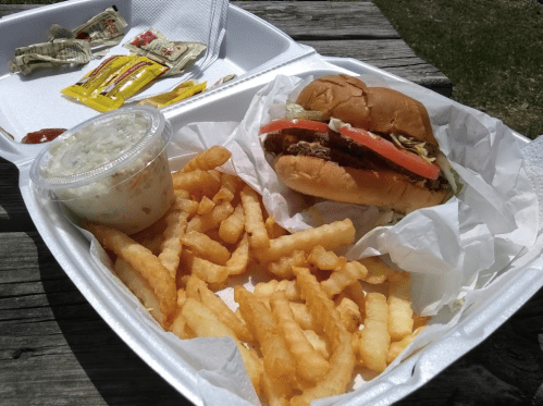 A takeout meal featuring a burger with lettuce and tomato, crinkle-cut fries, and a side of coleslaw.