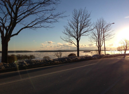 A serene winter landscape with bare trees, a river, and a sunset casting warm light over the scene.