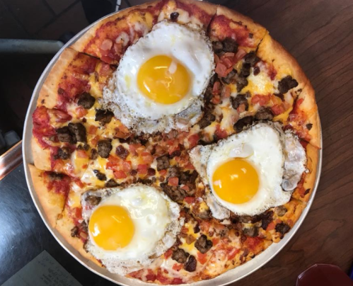 A pizza topped with ground beef, tomatoes, cheese, and three sunny-side-up eggs on a golden crust.