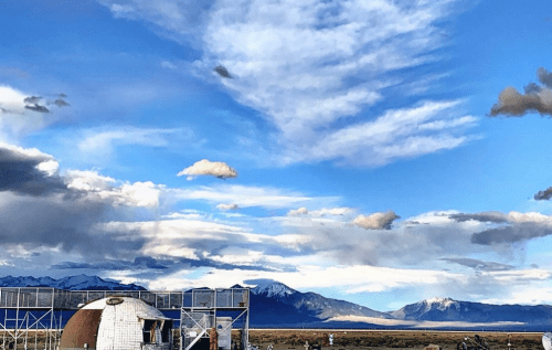 A scenic view of mountains under a blue sky with clouds, featuring a structure in the foreground.