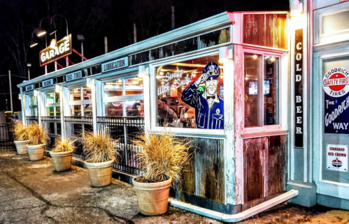 A retro-style diner with large windows, colorful lights, and potted plants outside, featuring a vintage mural.