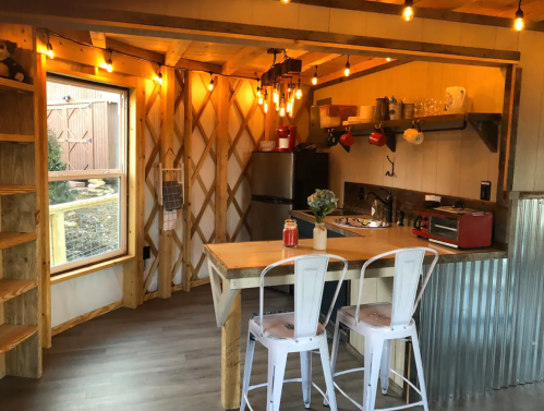 Cozy kitchen in a rustic cabin with wooden shelves, a dining table, and warm lighting.