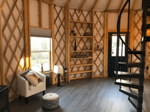 Cozy interior of a yurt featuring a spiral staircase, wooden shelves, and a comfortable seating area.