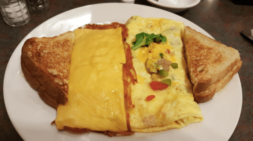 A plate with a cheese-covered omelet, hash browns, and two slices of toasted bread.