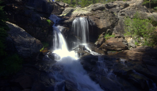 A serene waterfall cascading over rocky terrain, surrounded by lush greenery and sunlight filtering through the trees.