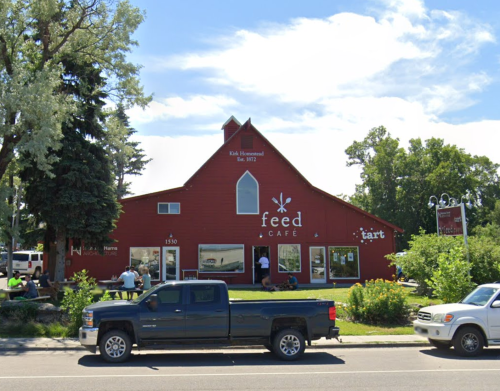 Red barn-style café with outdoor seating, surrounded by trees and parked cars. Sign reads "Feed Café."