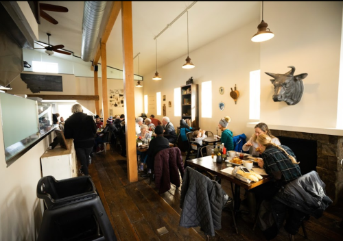 A cozy restaurant interior with diners at tables, wooden floors, and a decorative bull's head on the wall.