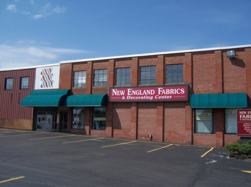 Exterior of New England Fabrics & Decorating Center, featuring a brick building with green awnings and a clear blue sky.