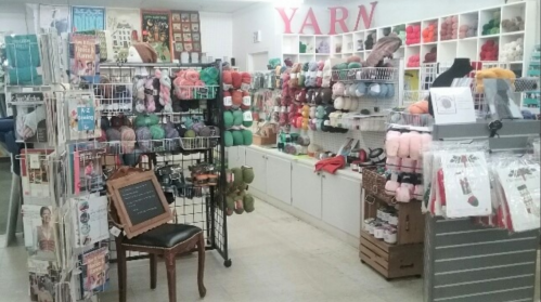 A cozy yarn shop filled with colorful yarns, knitting supplies, and displays of patterns and tools.