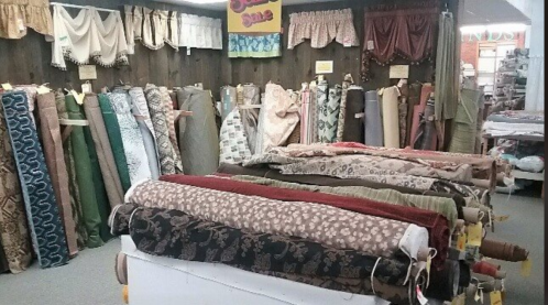 A fabric store displaying rolls of various patterned and textured fabrics on shelves and tables.