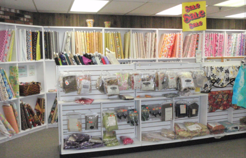 A fabric store display featuring colorful rolls of fabric and various sewing supplies on shelves. Sale signs are visible.
