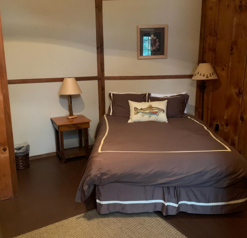 Cozy bedroom with a double bed, wooden walls, bedside table, lamp, and a decorative fish pillow.