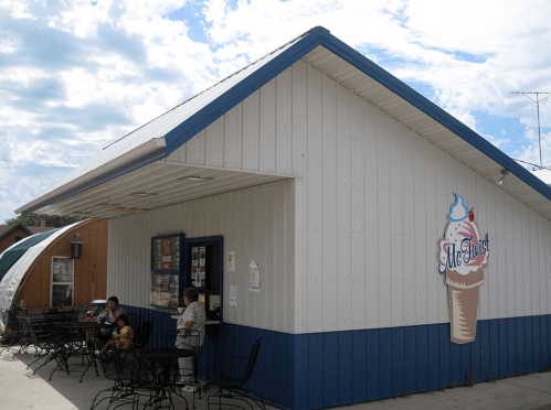 A small ice cream shop with a blue and white exterior, featuring outdoor seating and a large ice cream cone sign.