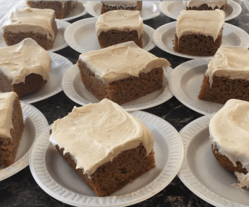 A close-up of square pieces of cake with frosting, arranged on white paper plates.