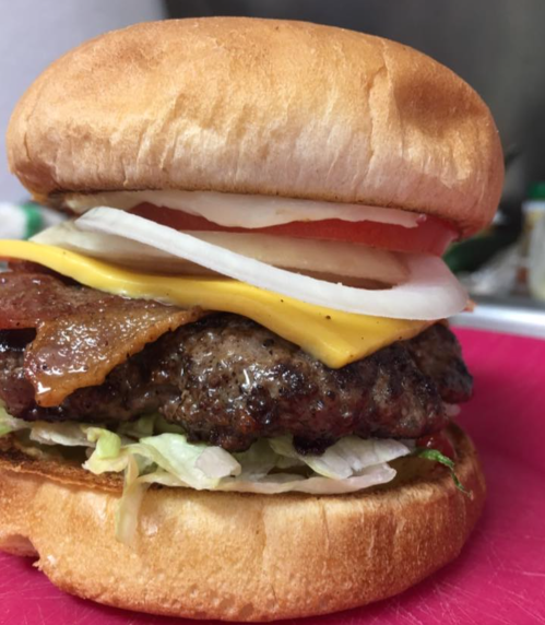 A close-up of a juicy hamburger with lettuce, tomato, onion, cheese, and bacon on a soft bun.
