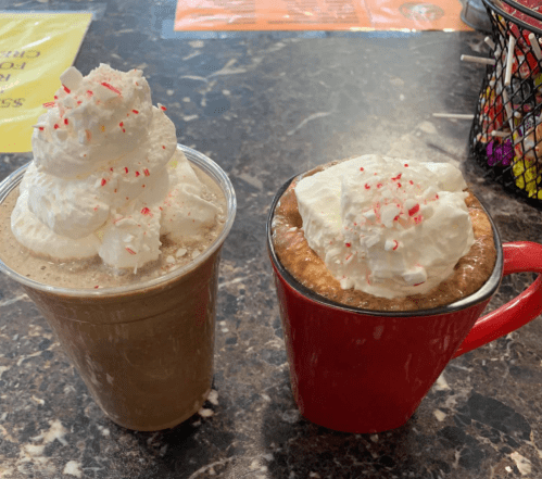Two festive drinks: a frosty beverage topped with whipped cream and crushed peppermint, and a hot drink in a red mug.