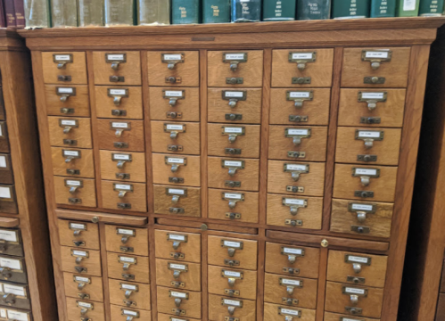 A wooden card catalog with multiple drawers, each labeled, in a library setting.