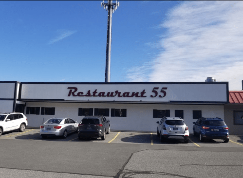 Exterior of Restaurant 55 with a clear sky, featuring parked cars in front and a cell tower in the background.