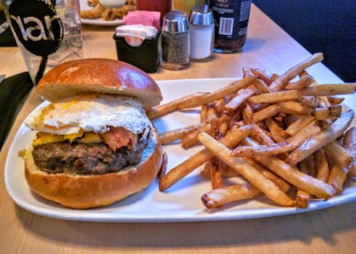 A juicy burger topped with an egg and bacon, served with a side of crispy French fries on a white plate.