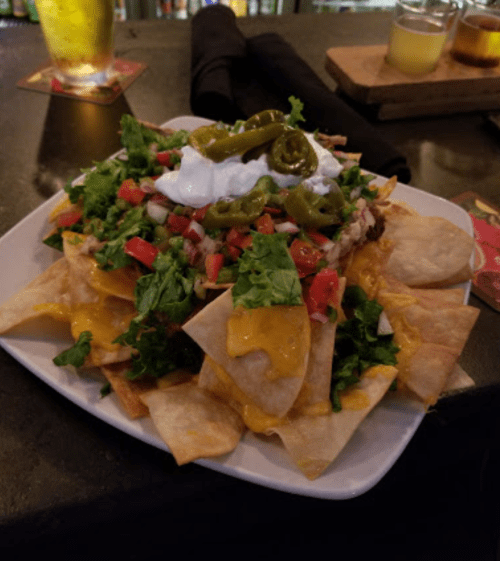 A plate of nachos topped with cheese, lettuce, tomatoes, jalapeños, and sour cream, served on a dark table.