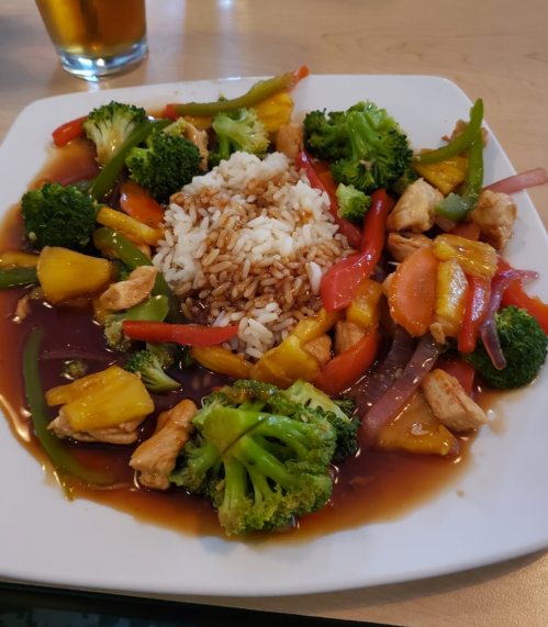 A plate of stir-fried chicken with broccoli, bell peppers, pineapple, and rice, served in a savory sauce.
