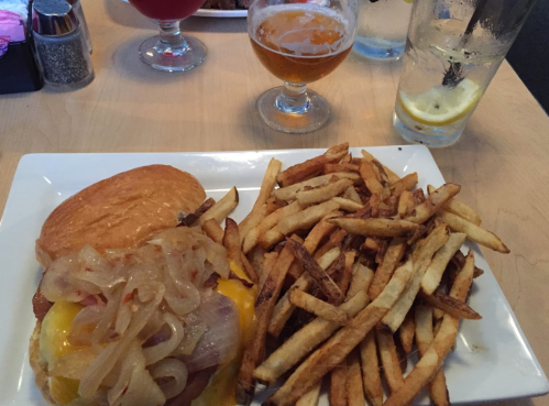 A plate with a cheeseburger topped with onions and a side of golden fries, accompanied by a glass of beer.
