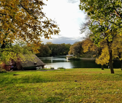 A serene lake surrounded by trees with autumn foliage and a quaint cottage in the foreground.