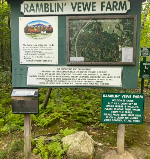 Sign at Ramblin' Vewe Farm with information about trails, wildlife, and visitor guidelines in a wooded area.