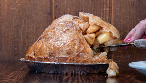 A freshly baked apple pie with a golden crust, partially sliced to reveal the warm apple filling inside.