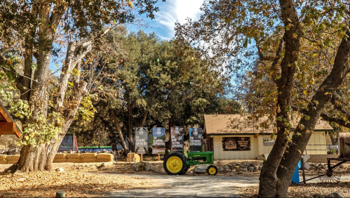 A rustic outdoor scene featuring a green tractor, trees, and a building with signs, surrounded by autumn leaves.