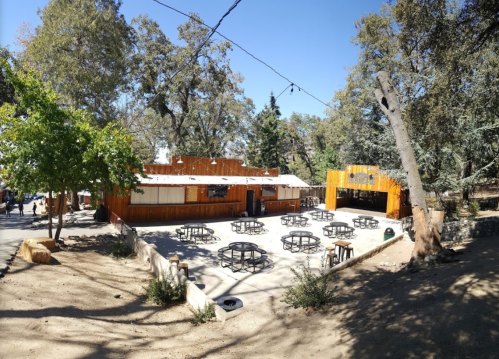 Outdoor venue with wooden structures, tables, and trees under a clear blue sky.