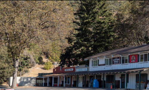A quaint street scene featuring rustic buildings, trees, and a clear blue sky in a rural setting.