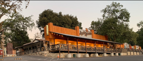 A rustic restaurant with wooden exterior and outdoor seating, surrounded by trees in a serene setting.