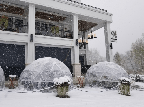 Snow-covered outdoor dining igloos in front of a restaurant, with heavy snowfall and winter scenery.