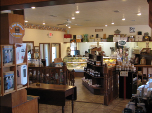 Cozy café interior with display cases, wooden furniture, and shelves filled with jars and baked goods.