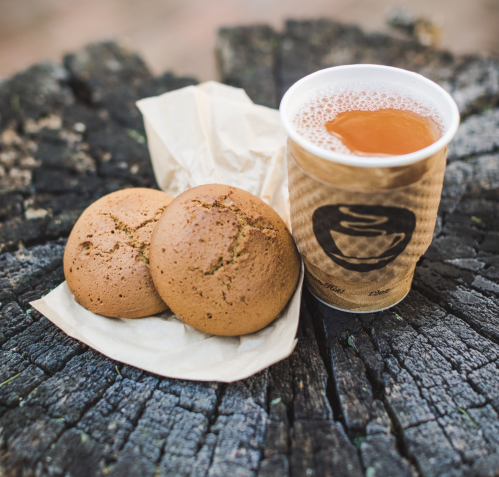 A cup of tea next to two cookies on a piece of parchment, resting on a wooden stump.
