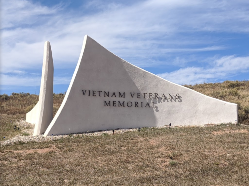 Vietnam Veterans Memorial sign with a modern design, set against a grassy landscape and blue sky.