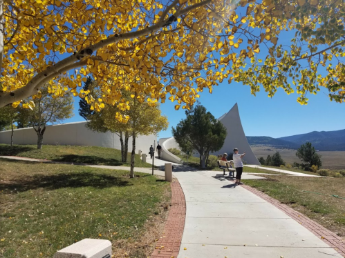 A sunny park scene with yellow leaves, a winding path, and people walking near a modern white structure in the background.