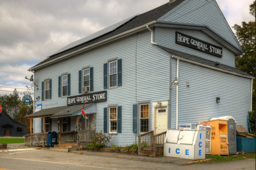A blue two-story building with "Hope General Store" signage, featuring a porch and a nearby ice vending machine.