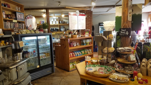 Cozy café interior with wooden shelves, snacks, a coffee station, and a display of baked goods.