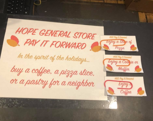 Sign promoting a "Pay It Forward" initiative at Hope General Store, offering free coffee, pizza slices, or pastries.