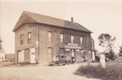Historic building with a vintage car parked outside, featuring wooden siding and a sign for a local business.