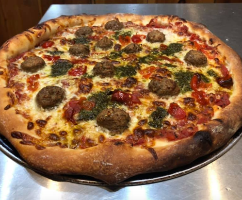 A freshly baked pizza topped with meatballs, cherry tomatoes, and pesto on a golden crust.